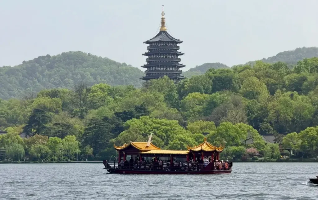 traditional boat on west lake hangzhou with pagoda and mountains in background