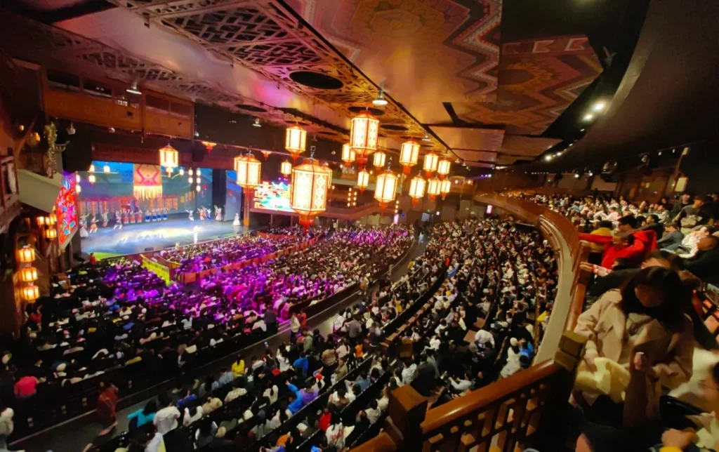 A capacity audience watching the large-scale Charming Xiangxi folk cultural performance on a brilliantly lit stage inside the ornately painted ethnic-style theater, Zhangjiajie, Hunan