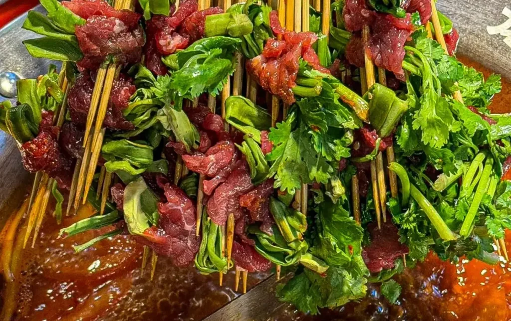 Chengdu chuanchuanxiang beef and cilantro skewers being dipped into bubbling spicy red chili broth