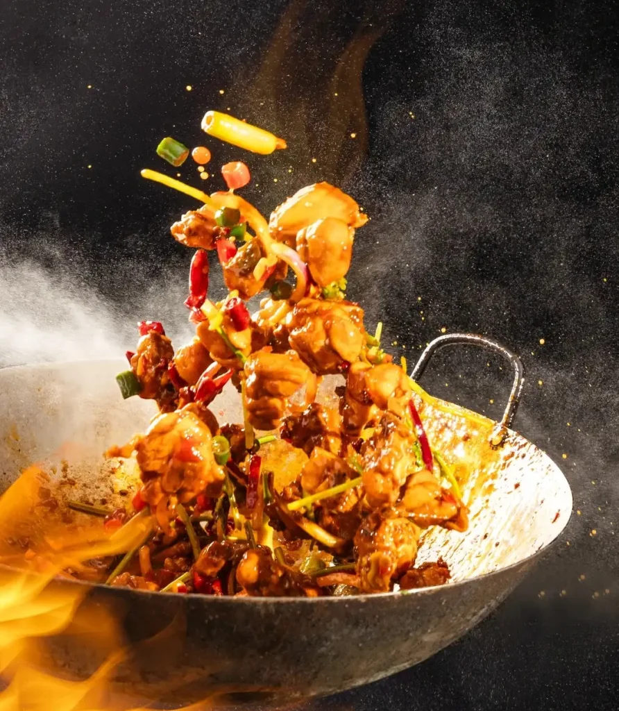 Professional food photography of Sichuan-style spicy wok-tossed chicken with chili peppers in a flaming iron wok