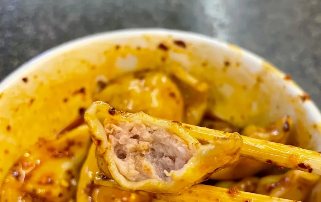 Chengdu Zhong Shuijiao pork dumplings in red chili oil sauce held by chopsticks classic Sichuan snack