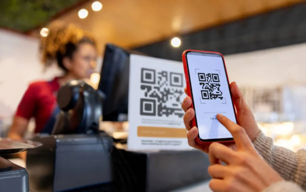 A customer scanning a QR code payment screen on their phone at a café counter in China