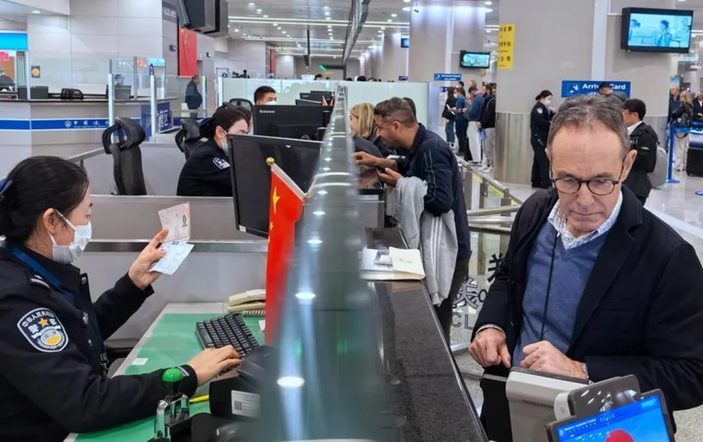 Foreign visitor completing passport check at a China visa-free entry counter in an international airport arrival hall