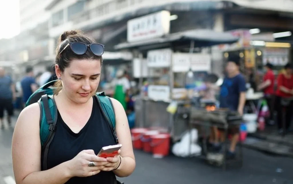 Female backpacker tourist using mobile internet on smartphone at China street food market