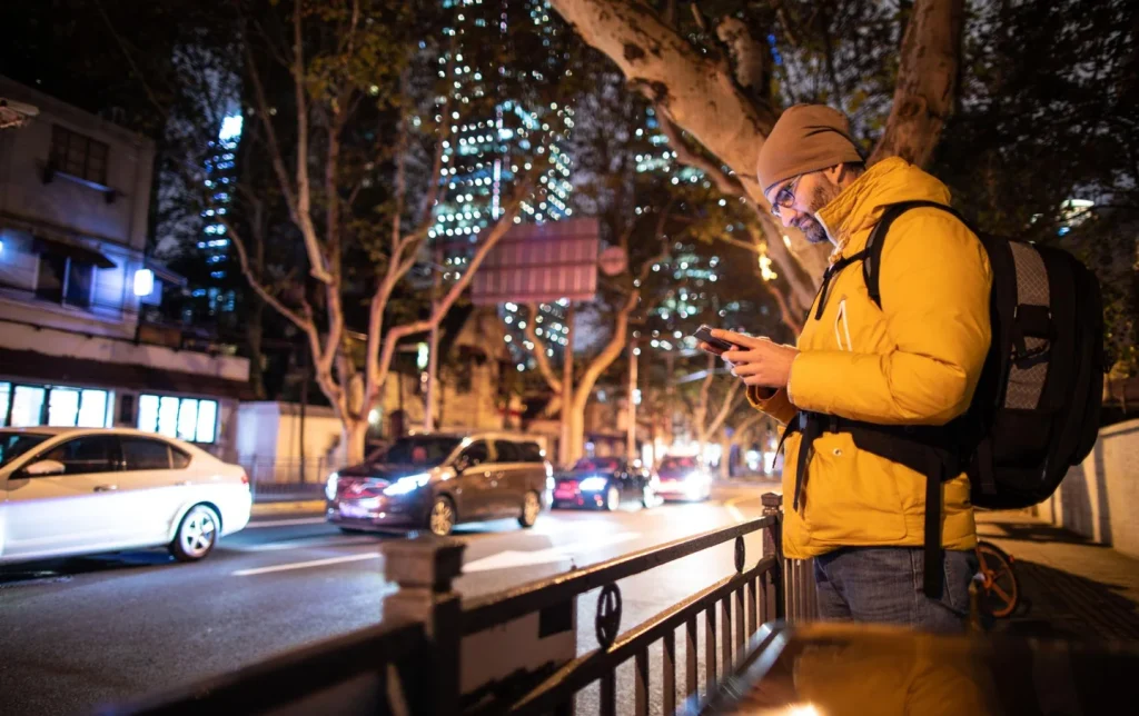 Foreign traveler in yellow jacket using smartphone on illuminated China city street at night