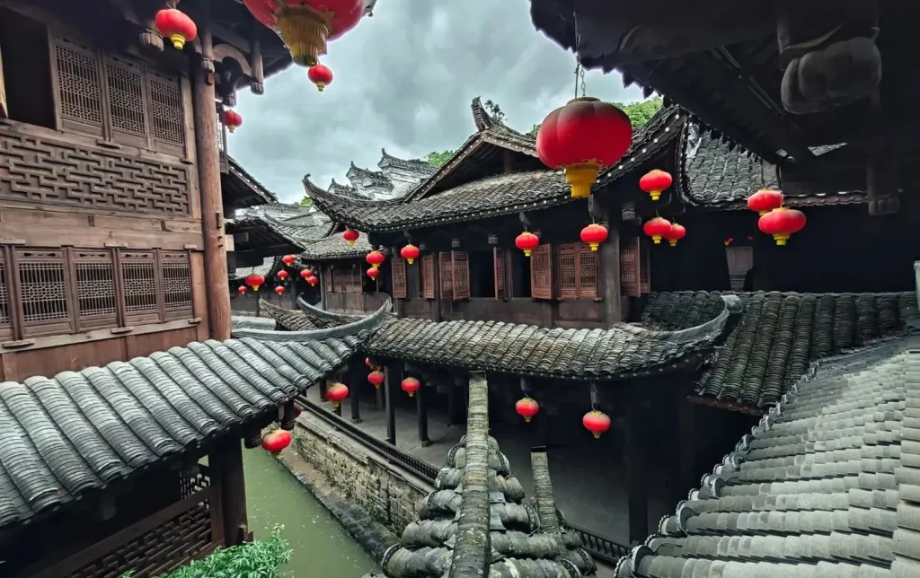 Intricately carved wooden lattice windows and curved upturned eaves of traditional Chinese architecture draped with red festival lanterns above a narrow water channel in Furong Ancient Town, Hunan