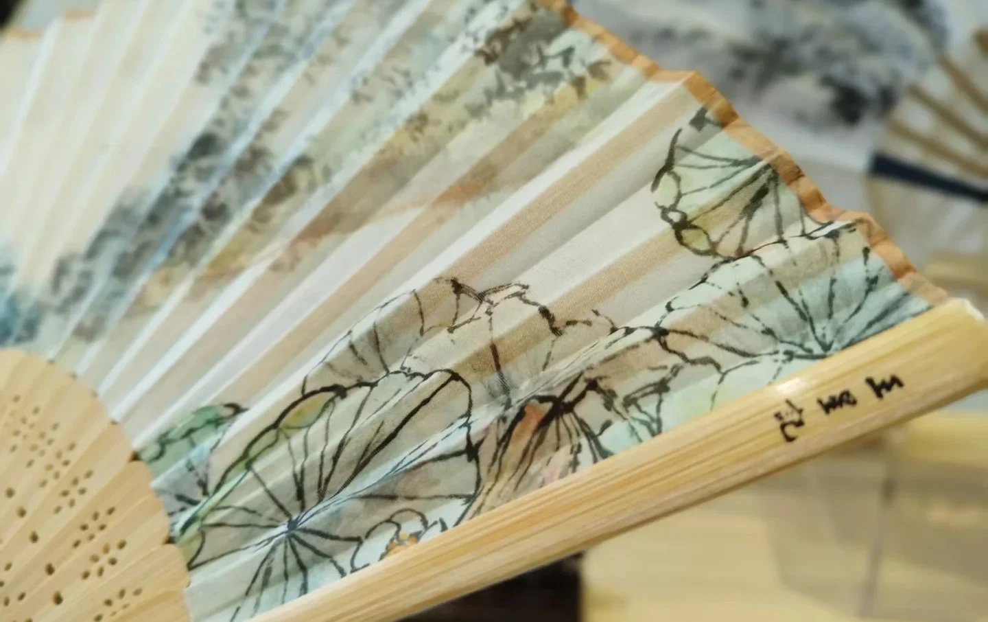 Close-up detail of a Wangxingji bamboo folding fan with delicate lotus ink painting — Hangzhou intangible cultural heritage fan craft