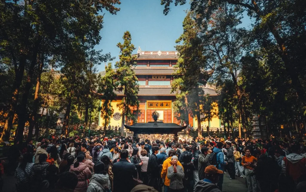 Large crowd of worshippers burning incense before the grand golden Daxiongbaodian hall of Lingyin Temple surrounded by ancient trees — Hangzhou Buddhist temple tour