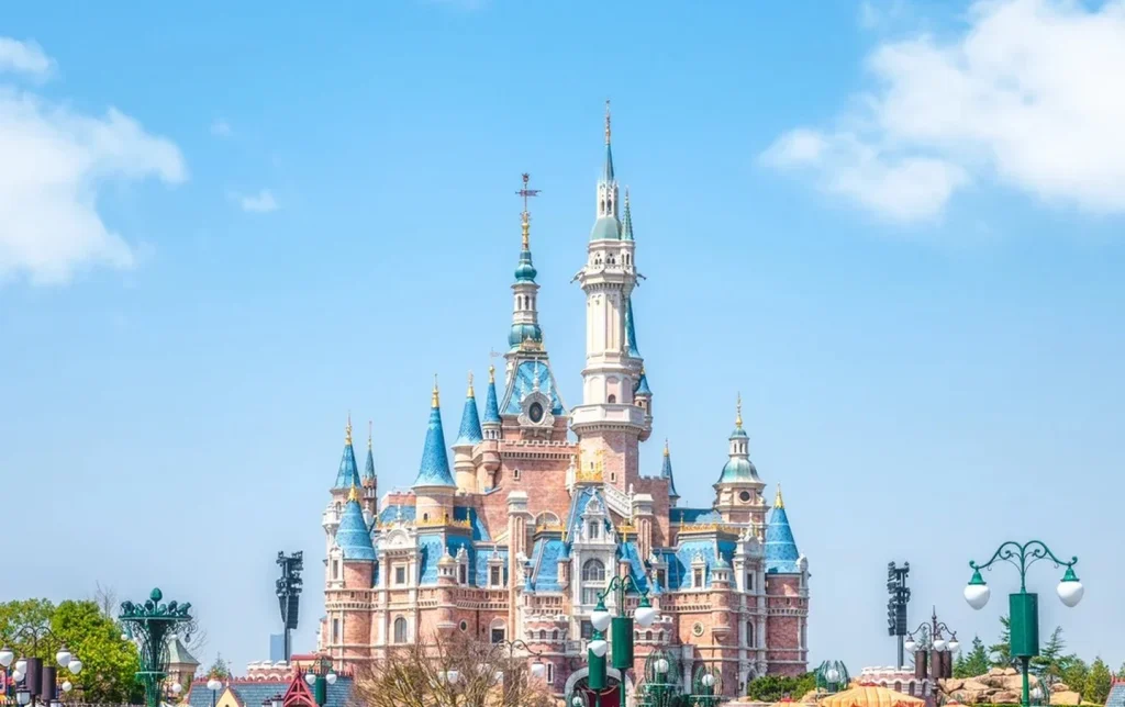 Shanghai Disneyland Enchanted Storybook Castle reflected in the lagoon on a bright blue-sky day with colorful flower beds — Shanghai Disney resort