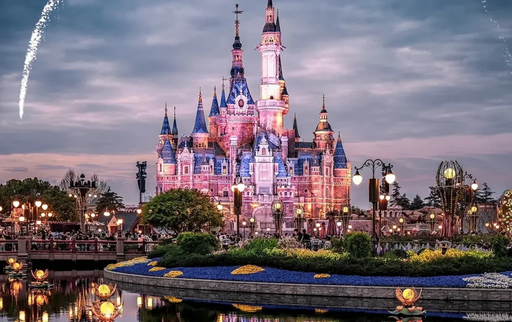 Shanghai Disneyland Enchanted Storybook Castle lit in pink and purple at night with a fireworks arc reflected in the lagoon — Shanghai Disneyland tour
