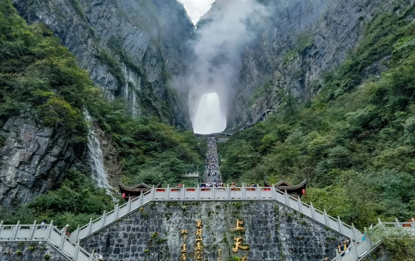 Visitors ascending the 999-step stairway toward Heaven's Gate arch at Tianmen Mountain, Zhangjiajie, with cliff faces draped in cloud sea on both sides