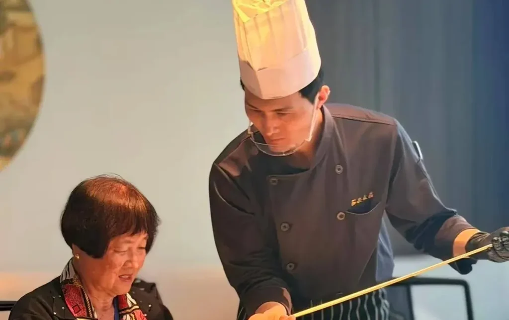 Chef in tall white hat teaching a foreign tourist how to hand-pull Biang Biang noodles during an authentic Xian culinary experience