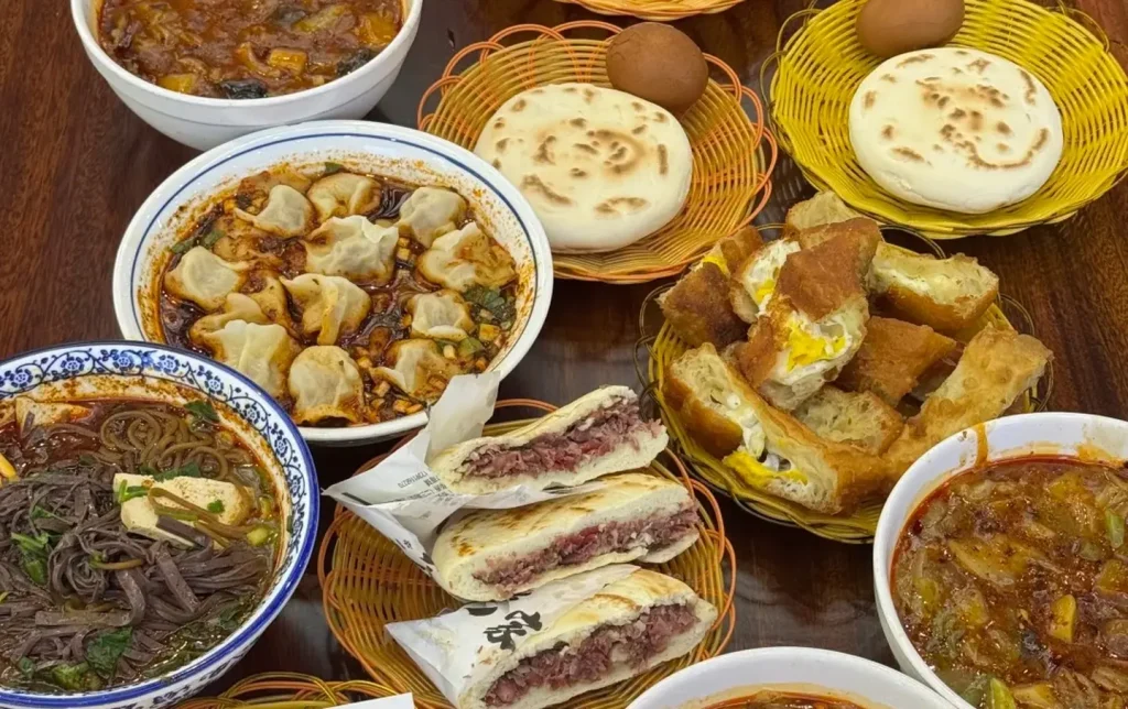 Authentic Shaanxi breakfast spread featuring roujiamo meat sandwiches, noodle soups, and dumplings, traditional Xian food tour for international visitors