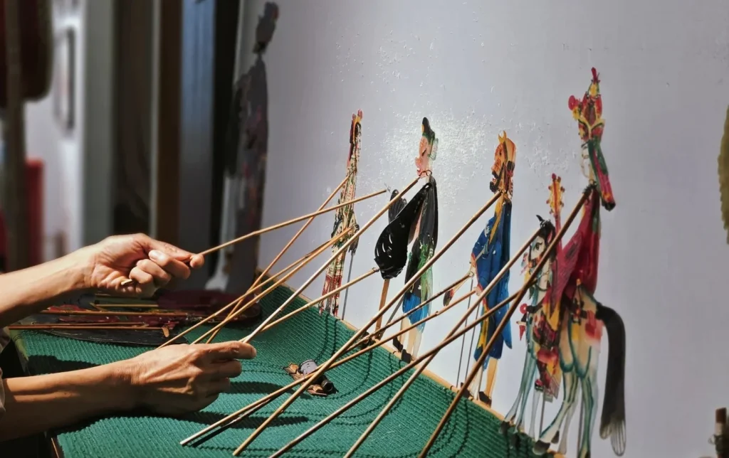 Artisan's hands manipulating multiple colorful leather shadow puppet figures on bamboo rods during a traditional piyingxi (shadow puppet) performance, Xi'an intangible cultural heritage