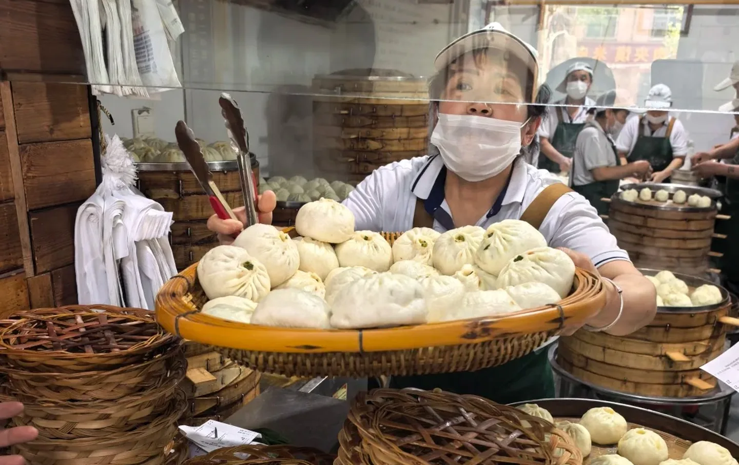 Street food vendor presenting a large basket of freshly steamed baozi buns at a busy Xian food market, authentic China street food experience