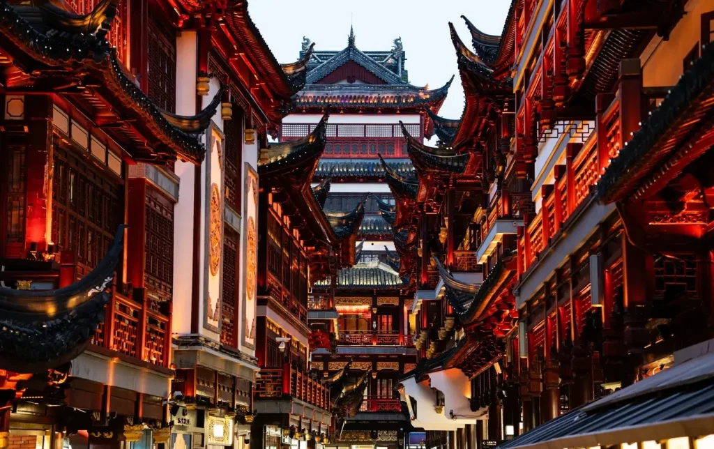 Looking up at the layered red-and-black traditional rooflines of Yuyuan City God Temple bazaar lit up at dusk — Shanghai Yuyuan night visit