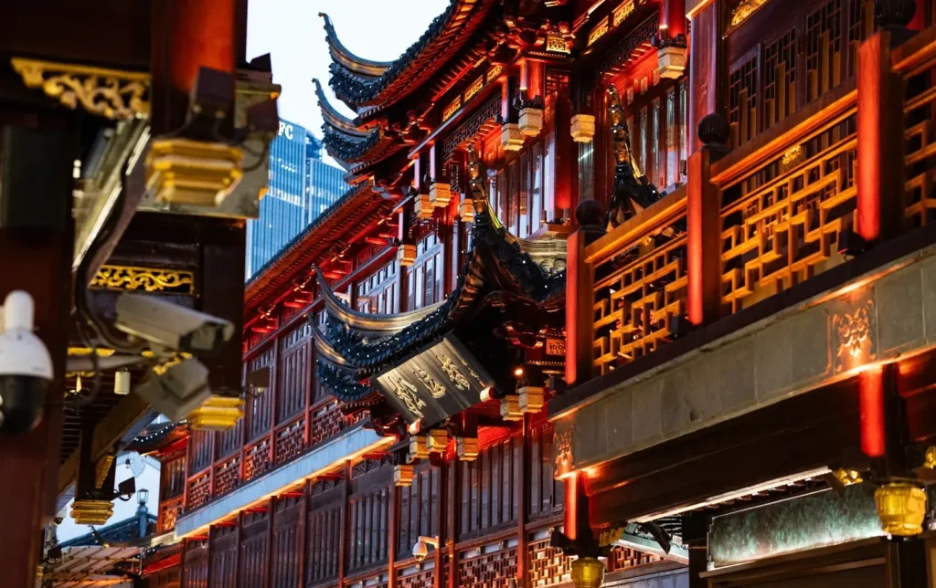 Close-up of Yuyuan Temple's sweeping curved roof eave lit red at night with a modern skyscraper visible behind — Shanghai old meets new