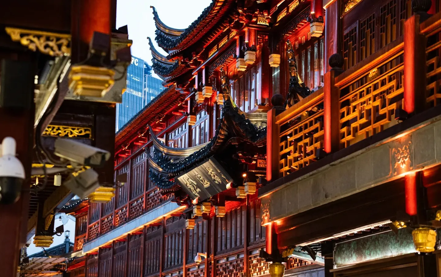 Close-up of Yuyuan Temple's sweeping curved roof eave lit red at night with a modern skyscraper visible behind — Shanghai old meets new