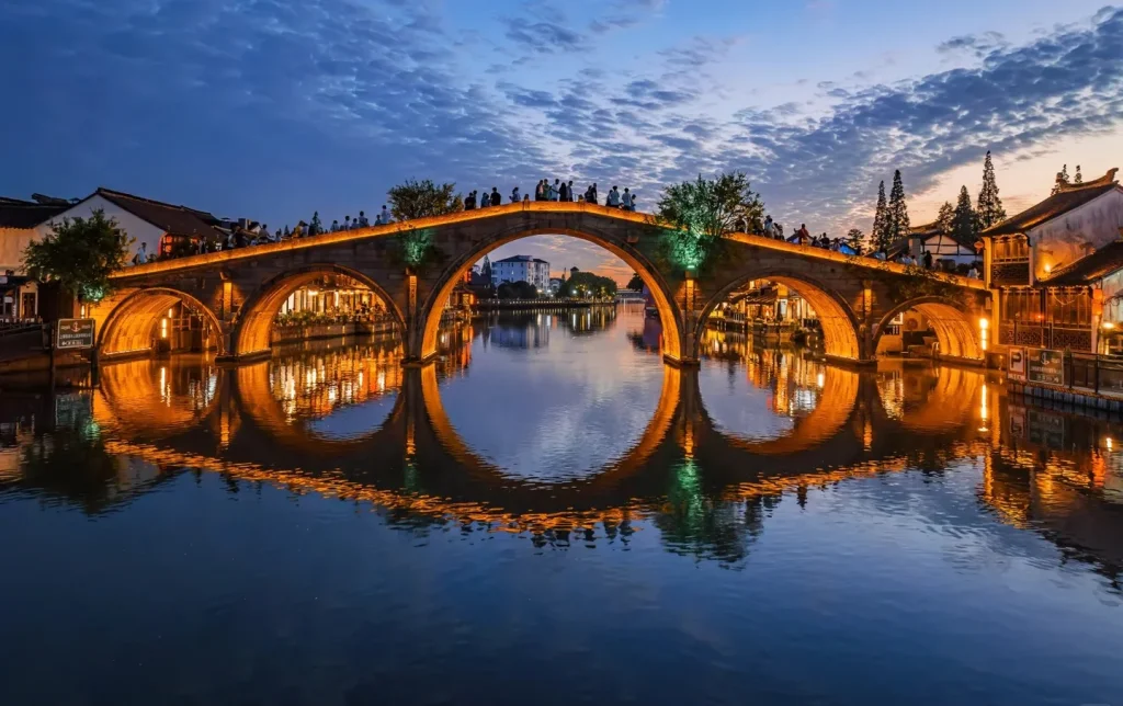 Zhujiajiao ancient water town illuminated stone arch bridge with perfect canal reflection at night