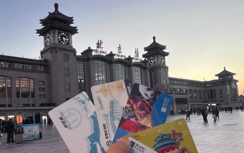 A hand holding multiple Beijing transit and subway cards in front of Beijing Railway Station at dusk, a practical guide to getting around on Beijing tours