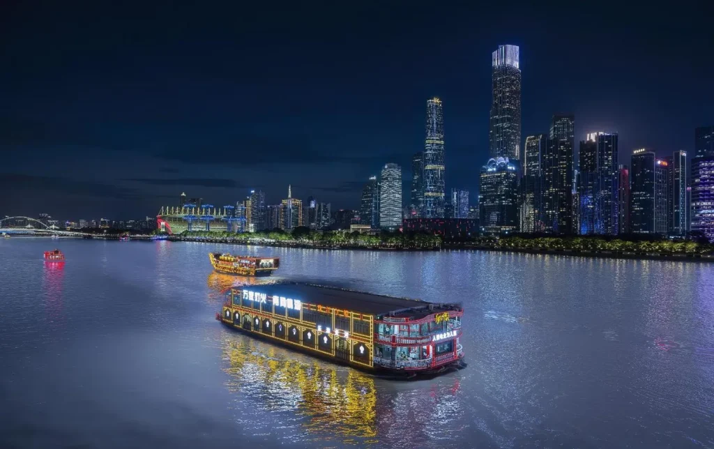 Illuminated traditional-style cruise boat sailing on the Pearl River at night with the Guangzhou skyline in the background, a highlight of Guangzhou night tour packages