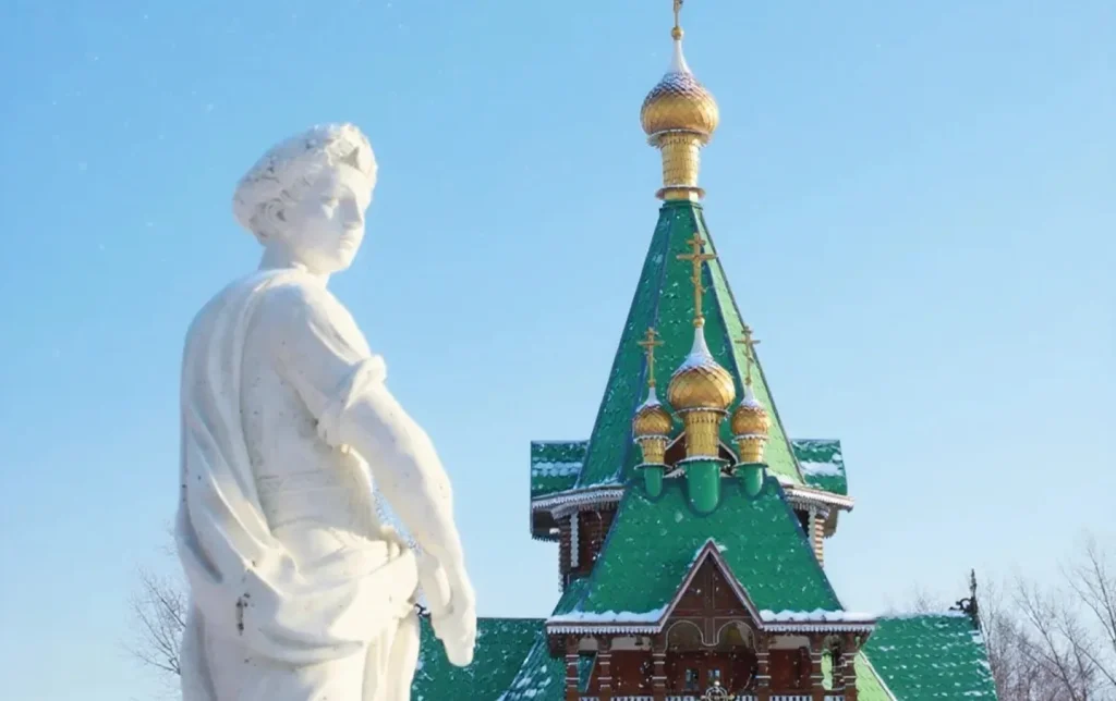 A marble statue before a snow-covered Russian Orthodox wooden church with golden domes against a blue sky in Harbin, a signature sight on Harbin winter tours